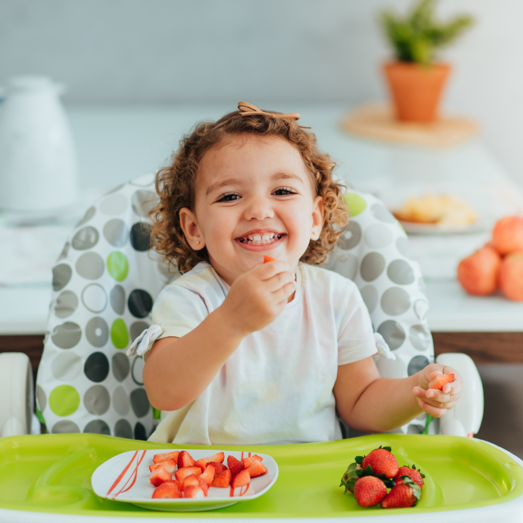 young girl eating strawberries in highchair